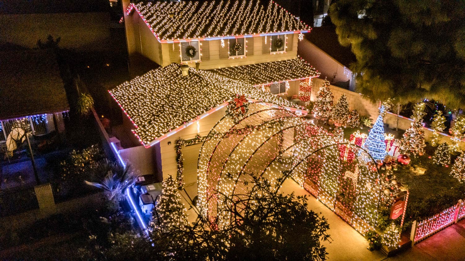 Large residential property transformed with a coordinated warm white and red holiday lighting display