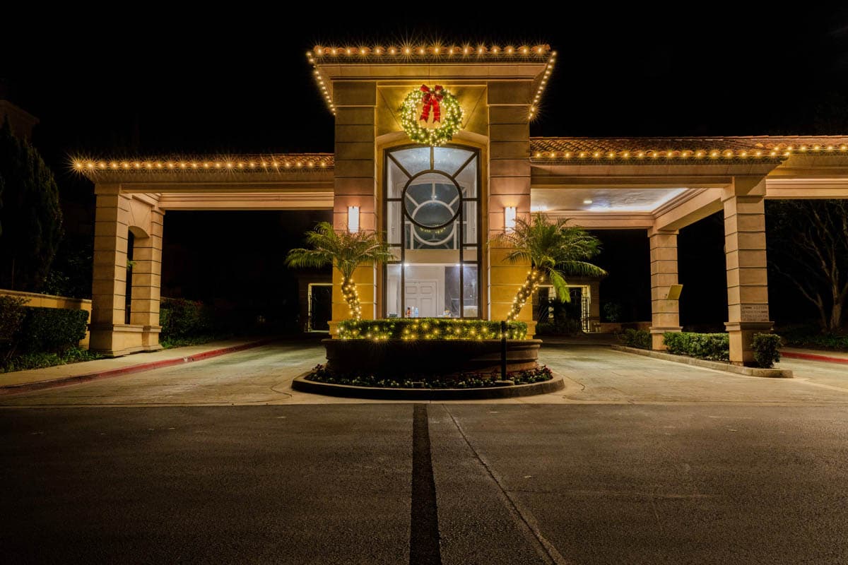 Formal commercial arrival pavilion outlined with warm white holiday lights and a centered wreath