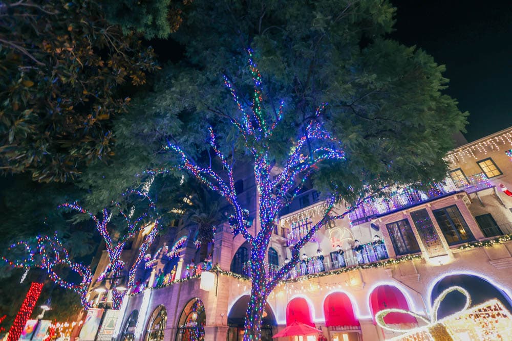 Large outdoor commercial destination with trees and façades illuminated in coordinated multicolor holiday lighting