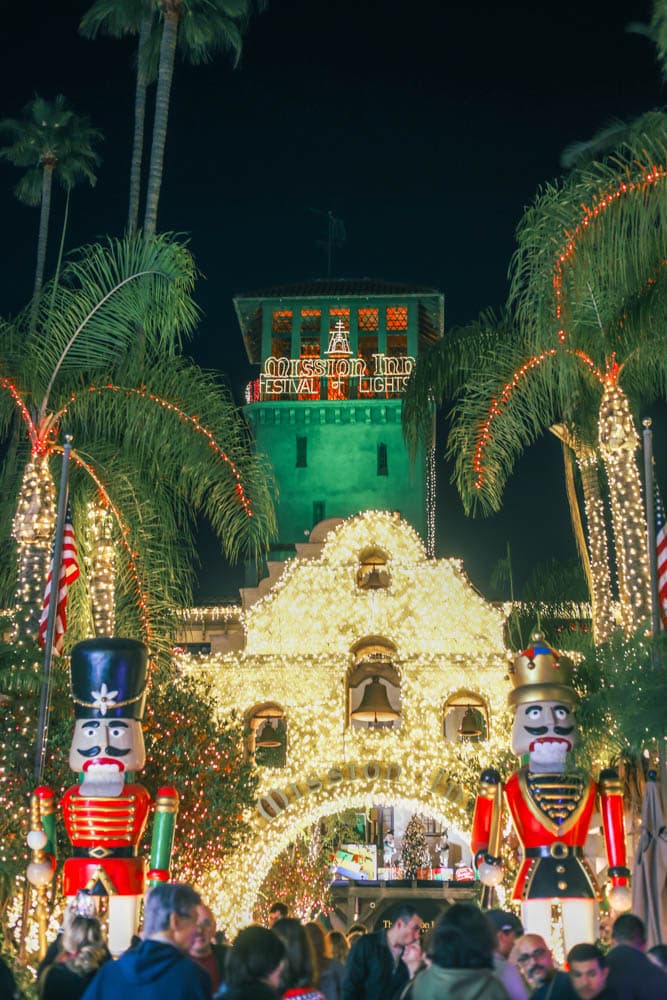 Large public holiday entrance glowing with thousands of warm white lights, nutcrackers, palms, and crowds