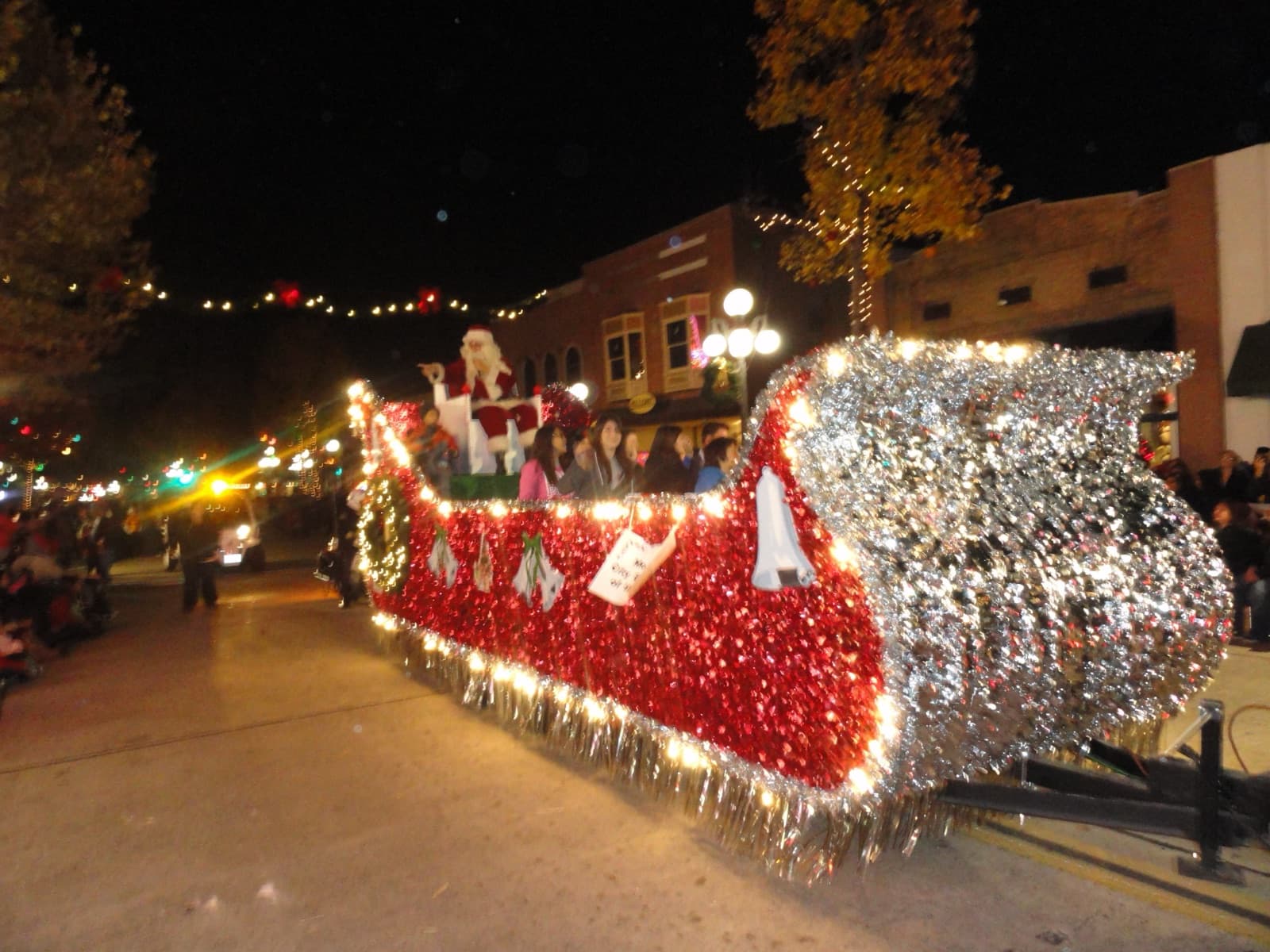 A Santa float covered in red silver and white lights on Myrtle Avenue at night