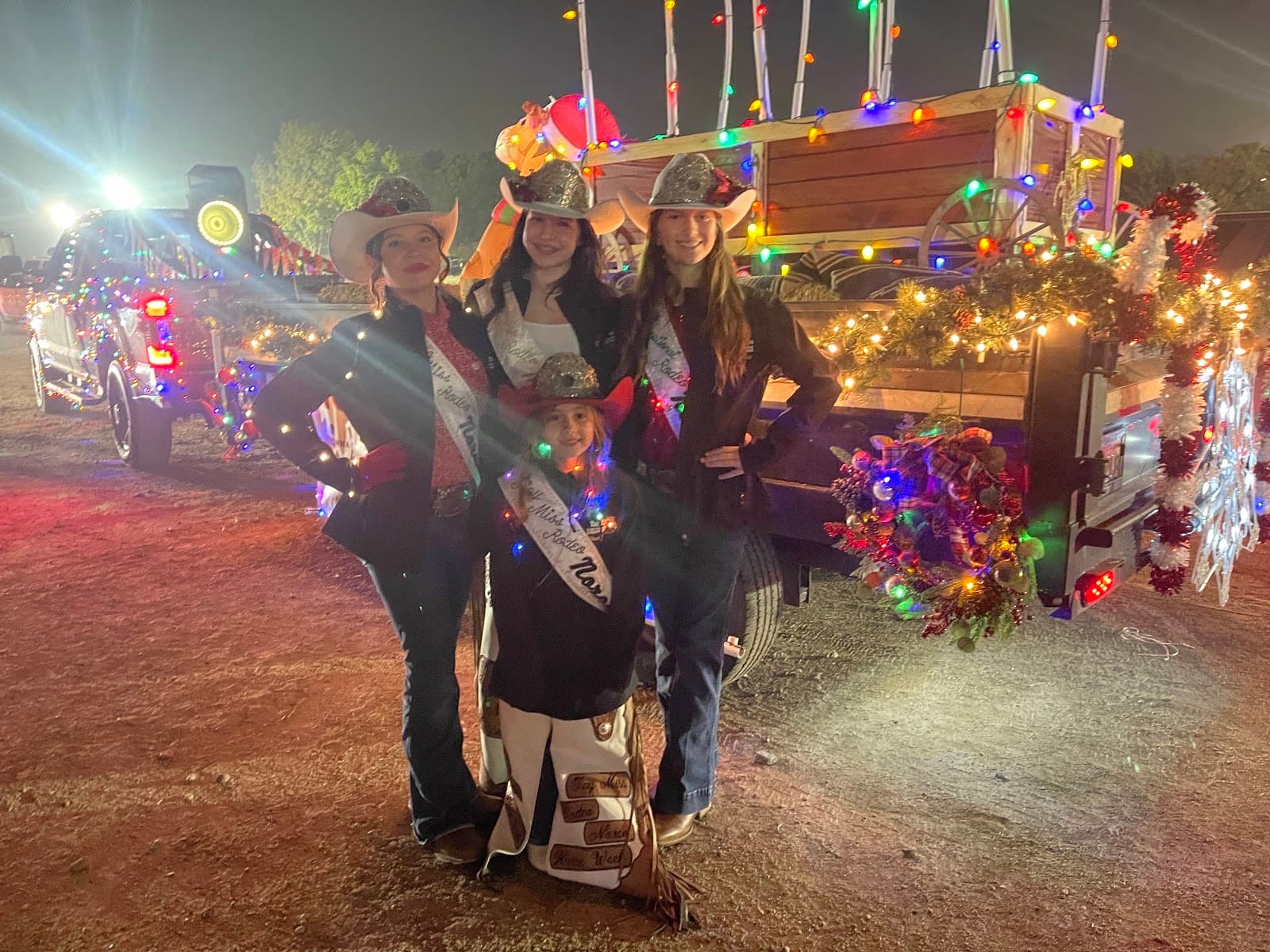 Norco parade riders posing beside a western wagon and vehicle covered in colorful Christmas lights