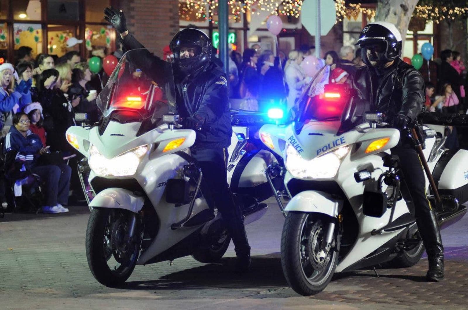 Police motorcycles leading the Seal Beach Christmas Parade beneath holiday lights at night