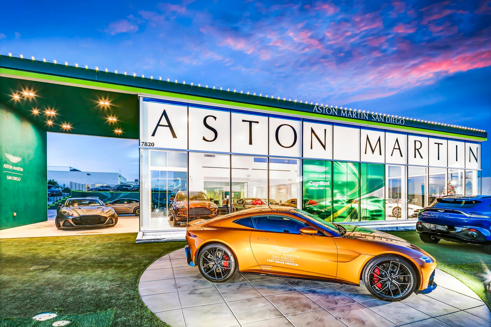 Orange Aston Martin displayed in front of an illuminated dealership showroom