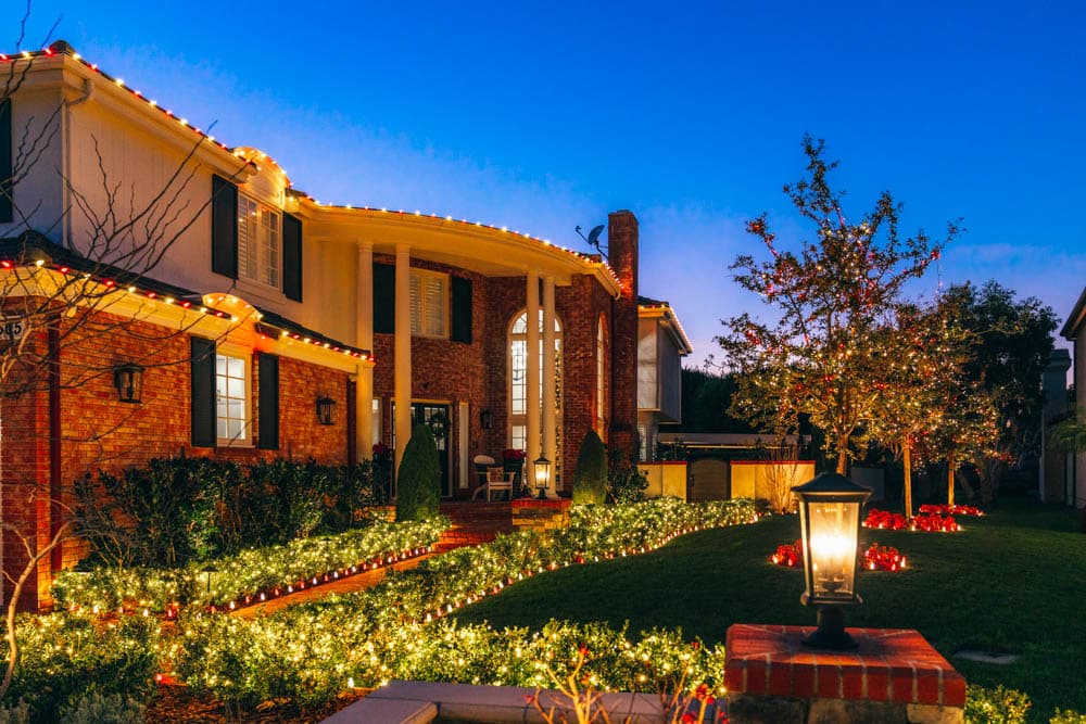 Traditional two-story residence with warm white and red roofline, tree, and garden lighting in the HLI portfolio